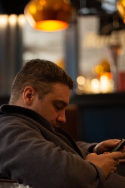 Bir adam kafede bir masada oturuyor ve telefona bakıyor. 
