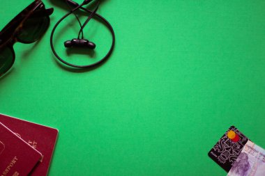 Konsept: seyahat. Yeşil arka planda pasaportlar, telefon, kulaklık ve kredi kartı var. 