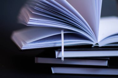 Siyah arka planda bir yığın kitap var. Onların üzerinde açık bir kitap vardır. 