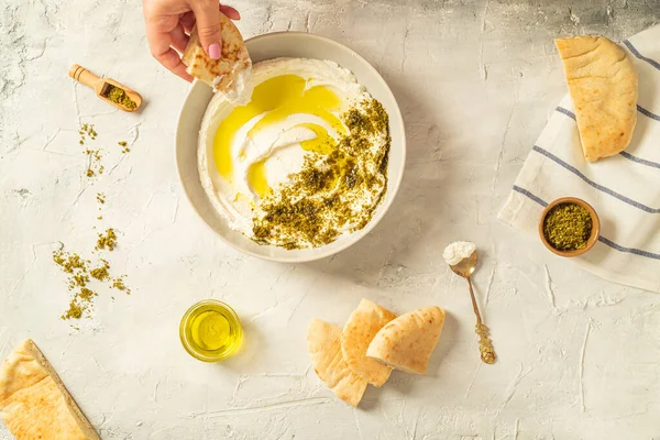 Popular Oriente Medio aperitivo labneh o labaneh, queso de leche de cabra blanca suave con aceite de oliva, hisopo o zaatar, servido con pan de pita sobre la mesa gris, flaylay. — Foto de Stock