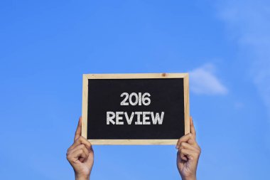 2016 REVIEW / Man mavi gökyüzü arka planında küçük bir karatahta tutuyor