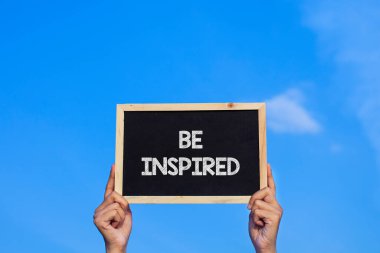 Mavi gökyüzü arka planında küçük bir karatahta tutan adam