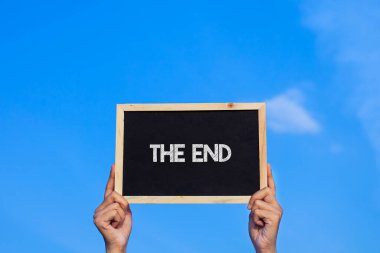 The End / Man mavi gökyüzü arka planında küçük bir karatahta tutuyor