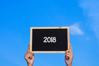 2018 / Man mavi gökyüzü arka planında küçük bir karatahta tutuyor