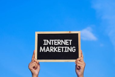 INTERNET MARKETING / Man mavi gökyüzü arka planında küçük bir karatahta tutuyor