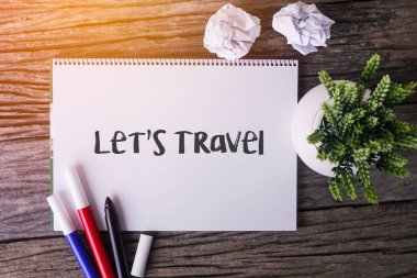 Notepad ve yeşil bitkiyle ahşap arka planda seyahat edelim.