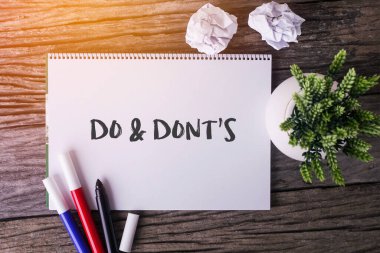 Do And Don 't' s word with Notepad and green plant on wood background