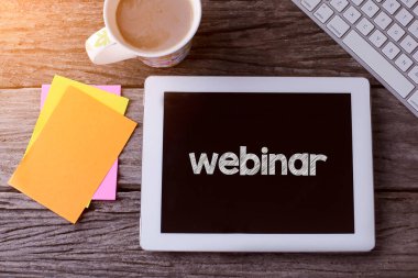 Webinar tableti ve ahşap arka planda bir fincan kahve.