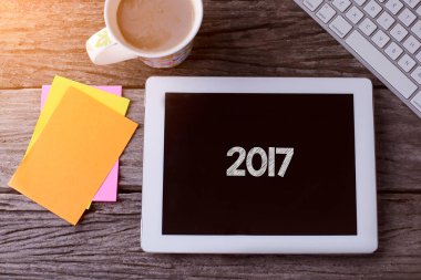 2017 numaralı tablet ve ahşap arka planda bir fincan kahve.