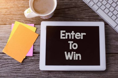 Enter To Win tableti ve tahta arka planda bir fincan kahve.