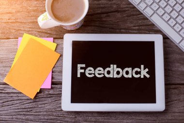 Geribildirim içeren tablet bilgisayar ve tahta arka planda bir fincan kahve.