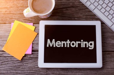 Akıl hocalığı yapan bir tablet bilgisayar ve tahta arka planda bir fincan kahve.