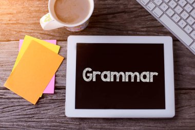 Gramer bilgisi olan bir tablet ve ahşap arka planda bir fincan kahve.