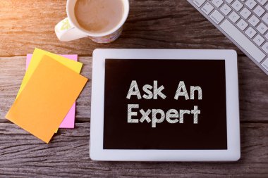 Ask An Expert ile tablet bilgisayar ve tahta arka planda bir fincan kahve.