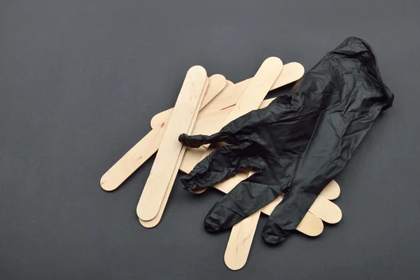 Guante negro y espátulas de madera para cera sobre negro. Preparación para — Foto de Stock