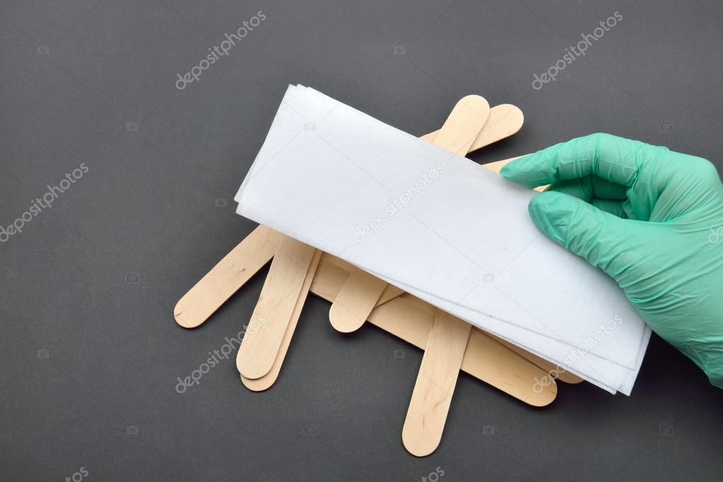 Beauticians hand with green glove holding paper tape for wax dep