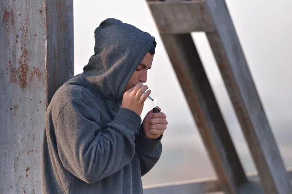 Junger Mann mit Kapuzenpullover steht an einer Brücke und zündet sich ein C an — Stockfoto