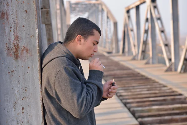 Jovem vestindo um capuz de pé por uma ponte e iluminando um c — Fotografia de Stock