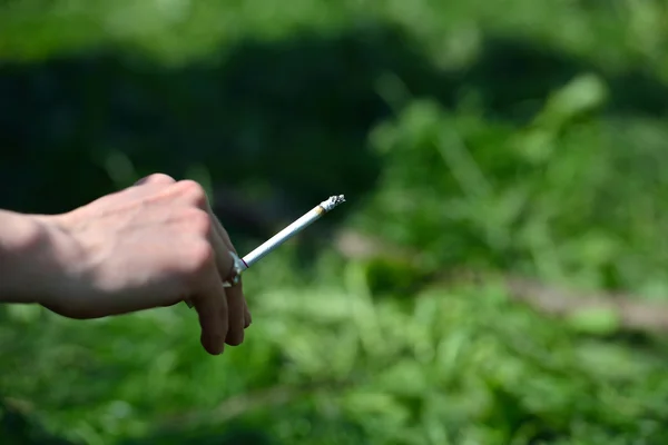 Yeşil çim arka plan c bir kadını elinde sigara — Stok fotoğraf