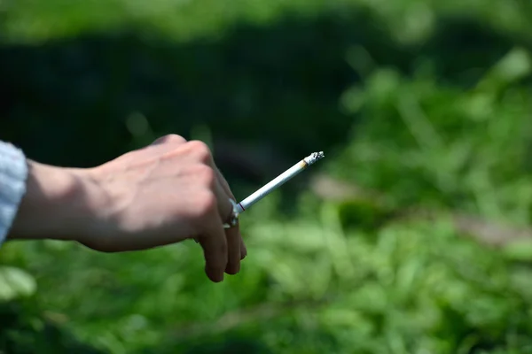 Cigarrillo en la mano de una mujer sobre el fondo de hierba verde c — Foto de Stock