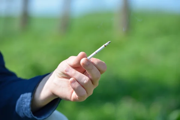 Bir sigara el dışında bir backgrou üzerinde tutan bir adamın elini — Stok fotoğraf