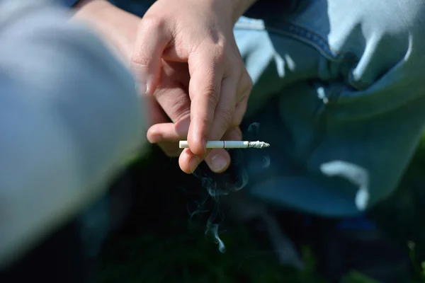 Mão de um homem segurando um cigarro na mão fora, em um backgrou — Fotografia de Stock