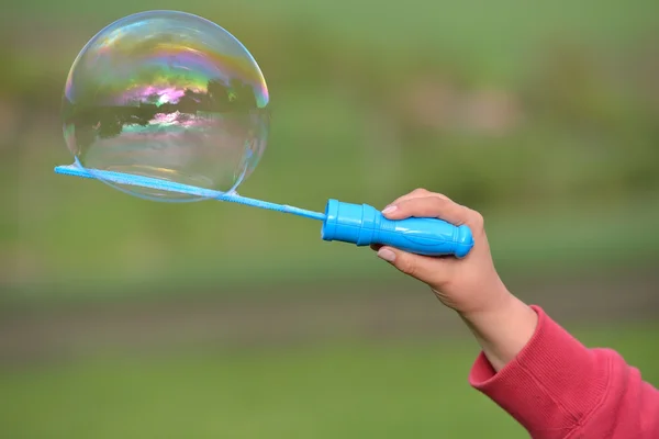 Close up of a soap bubble growing from the blower ring hold by a — Stock Photo, Image