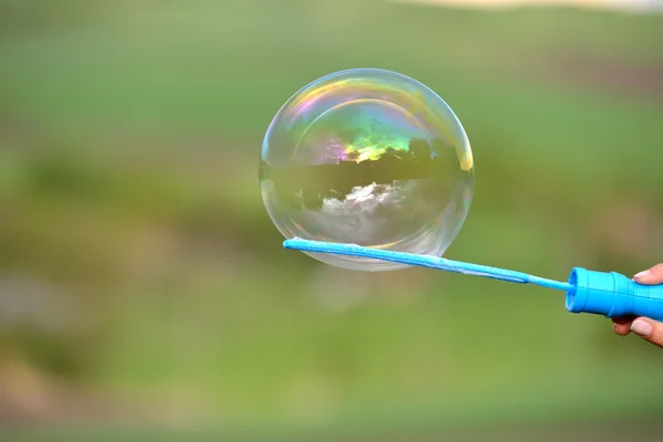 Close-up de uma bolha de sabão crescendo a partir do anel do ventilador segurar por um Fotos De Bancos De Imagens Sem Royalties