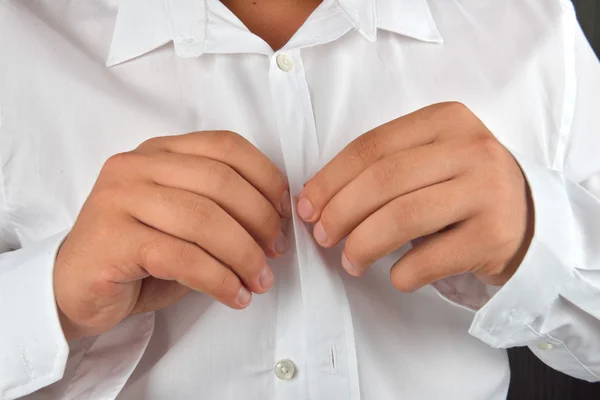 Young man buttoning his white shirt on a dark background. He is — Stock Photo, Image