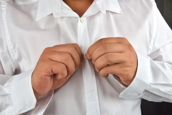 Jovem abotoando sua camisa branca em um fundo escuro. Ele é. — Fotografia de Stock