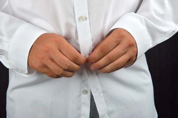 Hombre joven abotonando su camisa blanca sobre un fondo oscuro. Lo es. —  Fotos de Stock