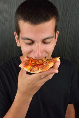 Aç gözlü genç adam yeme pizza karanlık bir arka plan üzerinde portresi