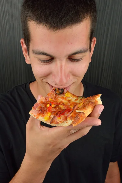Egy mohó fiatalember, eszik pizzát sötét háttér előtt portréja — Stock Fotó