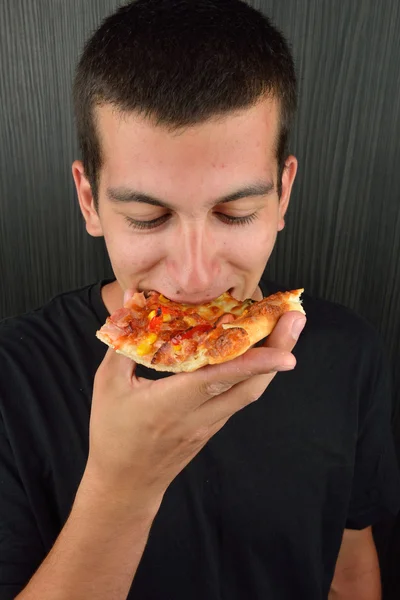 Aç gözlü genç adam yeme pizza karanlık bir arka plan üzerinde portresi — Stok fotoğraf