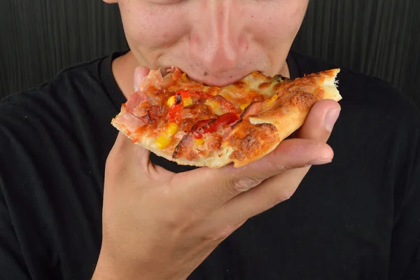 Retrato de un joven codicioso comiendo pizza sobre un fondo oscuro — Foto de Stock