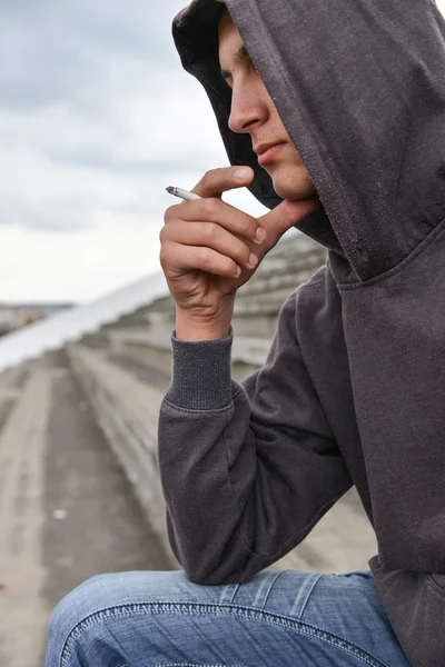 Young man in depression smoking a cigarette on a stadion. Concep — Stock Photo, Image