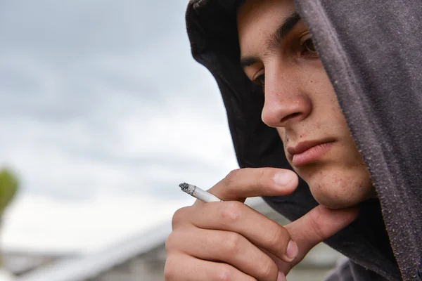 Menino adolescente pensativo e preocupado com capuz preto é fumar cigarro — Fotografia de Stock