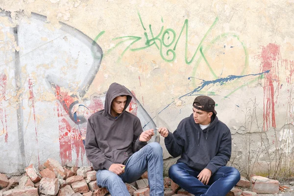 two street hooligans or rappers standing against a graffiti pain