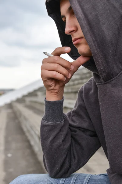 Jovem em depressão fumando um cigarro em um estádio. Concep Imagem De Stock