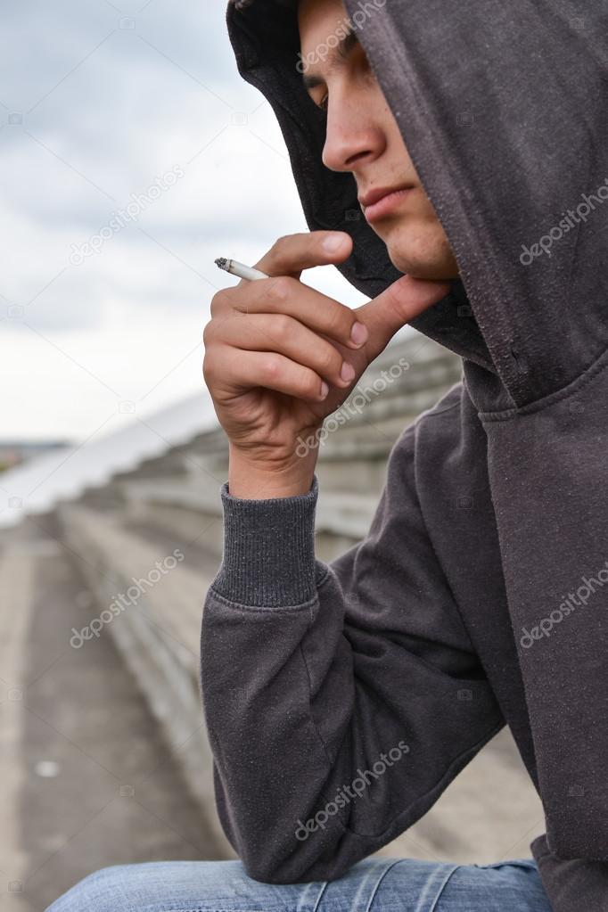 Young man in depression smoking a cigarette on a stadion. Concep