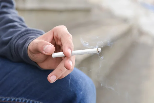 Homem segurando cigarro em sua mão fechar ao ar livre. Tiro cortado — Fotografia de Stock