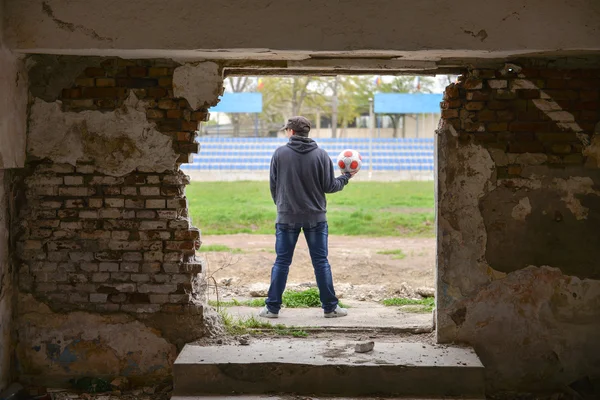 Genç adam ayakta bir futbol ile eski terk edilmiş binada bal — Stok fotoğraf