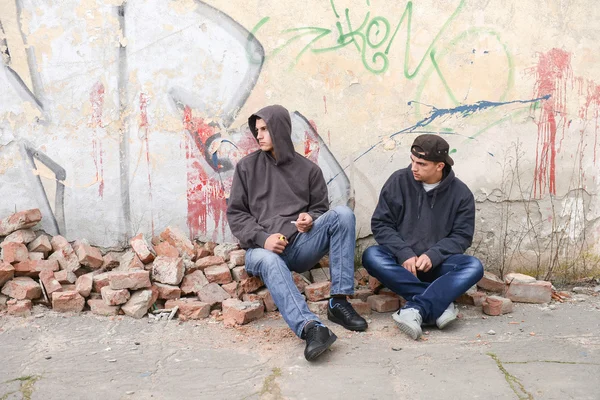 Two street hooligans or rappers sitting against a graffiti paint — Stock Photo, Image