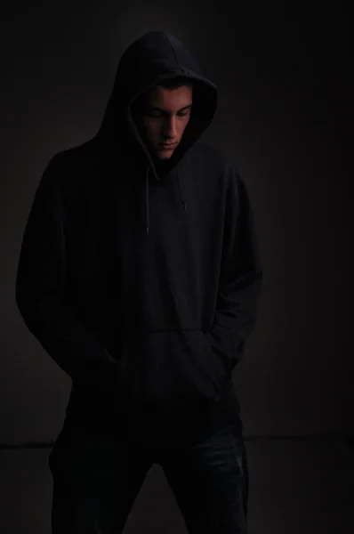 Tonåring med hoodie ser ner på svart bakgrund — Stockfoto