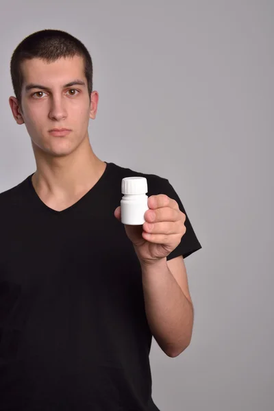 Mladý muž, který držel krabičku pilulek v ruce a ukazuje léky — Stock fotografie
