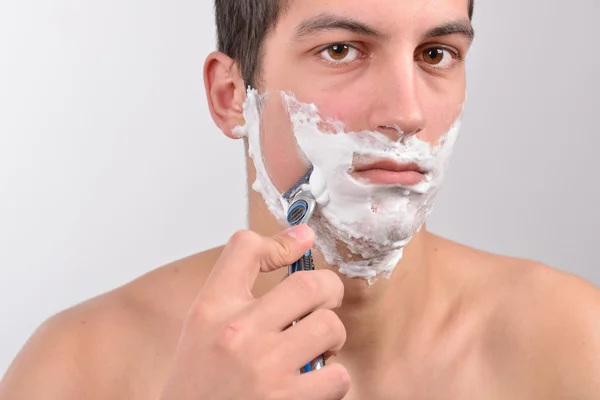 Handsome young man with lots of shaving cream on his face is sha