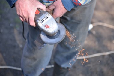 Bir adamın yakın elektrik değirmeni kullanarak bir balta keskinleştirmek. Sparks w