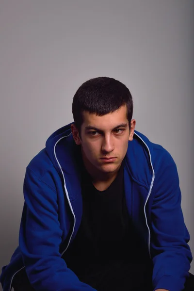 Sad teenager with blue sweatshirt standing against a dirty wall — Stock Photo, Image
