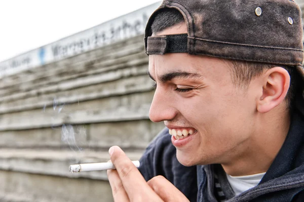 Imagen sobre fumar. joven se ríe y fuma un cigarro — Foto de Stock