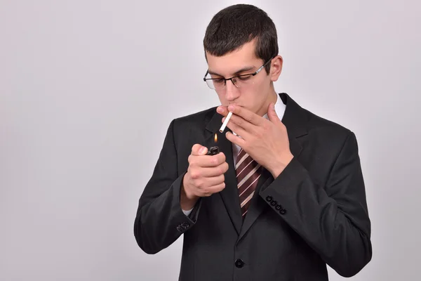 Young man dressed in tuxedo lighting cigarette in studio — Stock Photo, Image